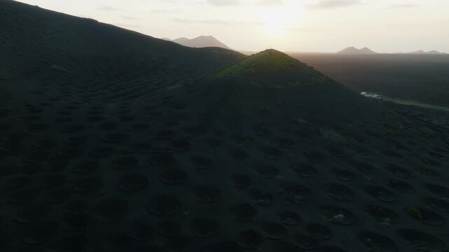 La Geria, Lanzarote, Spain, aerial drone shot of a volcanic hill at sunset, slowly arcing around the landscape as the sun sets behind it. Part 2