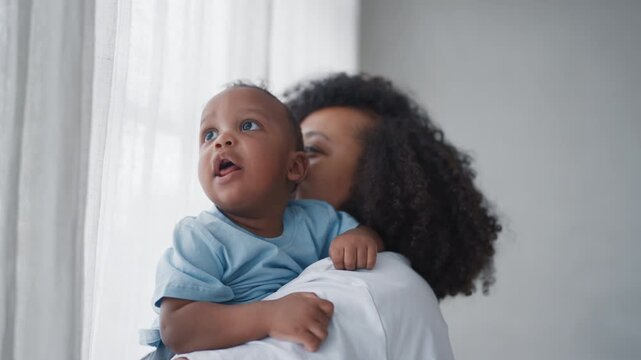 Portrait of cute little boy in hand of mother in cozy home interior, slow motion . Motherhood and childhood, pretty infant child looking around, exploring world, curious baby and happy mother at home