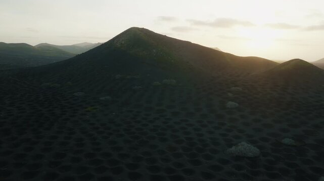La Geria, Lanzarote, Spain, aerial drone shot of a volcanic hill at sunset, slowly arcing around the landscape as the sun sets behind it. Part 1