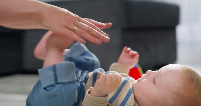A caregiver gently dressing a baby lying on the floor, focusing on the baby's legs and interactions during a playful and tender moment in a cozy indoor setting