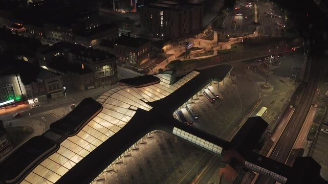 Night aerial view of Barnsley Interchange in Barnsley South Yorkshire England featuring illuminated transport canopy, bus station platforms and connected rail infrastructure, forward flyover