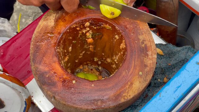 Making traditional indonesian crushed fruit salad known as rujak beubeuk inside a wooden mortar