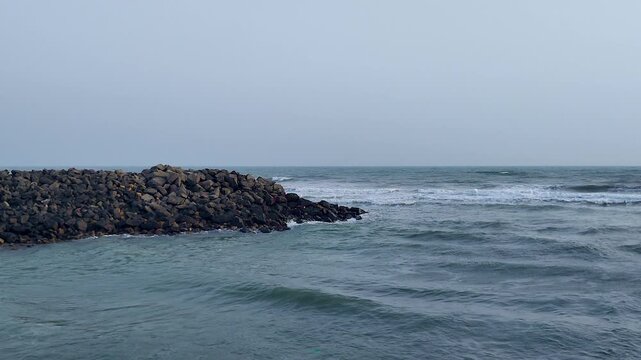 Rocky breakwater jetty meeting Arabian Sea waves at Dwarka, Ghomti Ghat, Gujarat. Ideal for Hindu pilgrimage, spiritual travel, India tourism, coastal infrastructure, and documentary projects.