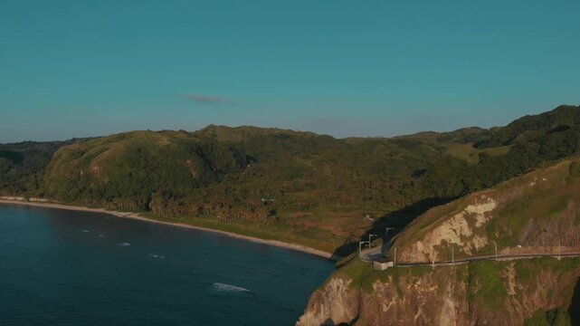 Aerial drone footage of Batanes Island in the Philippines, capturing its dramatic coastline, rolling hills, open sea, and peaceful island scenery. The shot highlights the natural beauty, remote charm,