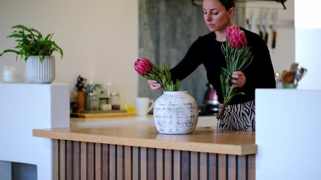 Woman arranging stunning pink proteas into a ceramic vase in a beautiful home
