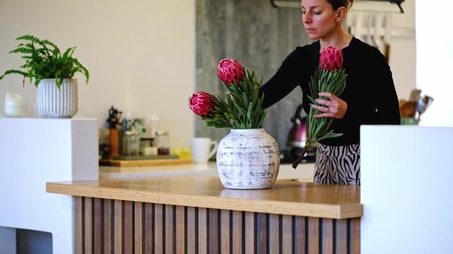 Woman placing pink proteas into a ceramic vase in her home