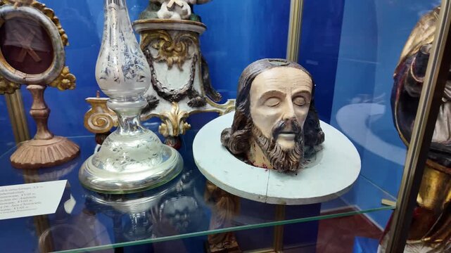 A carved wooden head of Saint John the Baptist presented on a wooden platter inside a museum showcase, filmed with a smooth left‑to‑right camera movement.