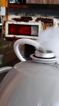 Close-up of liquid nitrogen vapor releasing from a metal container with a flexible hose attached.