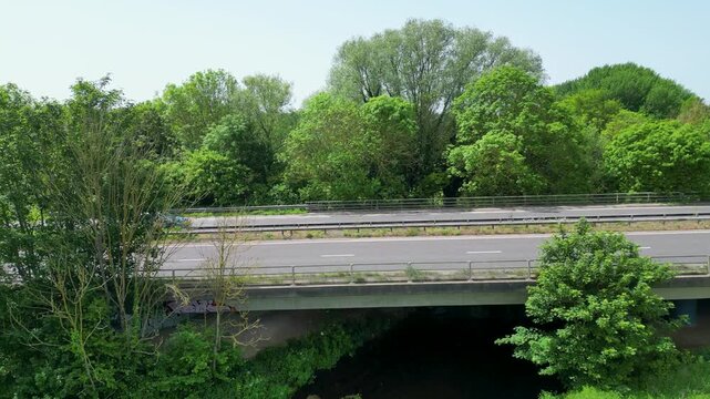 High Angle Aerial View of Traffic Crossing A2 Motorway Bridge Over Green Stream in Lush Woodland Hambrook Kent UK