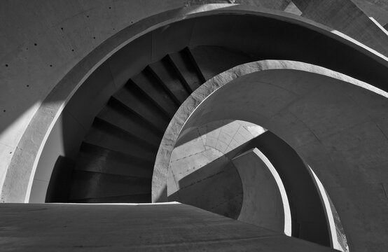 Dramatic black-and-white photograph of a spiral concrete staircase highlighting curved forms, strong shadows, and repeating geometric patterns for minimalist architectural and abstract design concepts