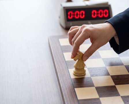 Hand Moving Chess Piece beside Digital Clock for International Chess Day and Endgame Pressure Concept