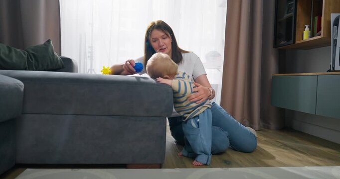 A mother plays and interacts with her toddler at home, supporting the child's early development and exploration through colorful toys in a cozy living room setting during daytime