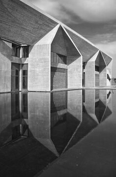 Brutalist concrete building with sharp geometric forms reflected in a still pool, captured in high-contrast black-and-white to emphasize texture, symmetry, light and shadow for a minimalist, dramatic