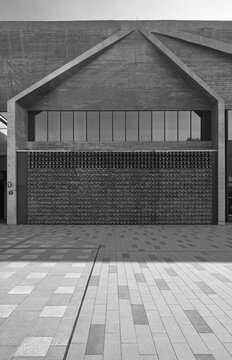 Minimalist concrete facade featuring bold geometric lines, textured brickwork and large windows overlooking a tiled plaza, conveying modern brutalist architecture, urban calm and architectural