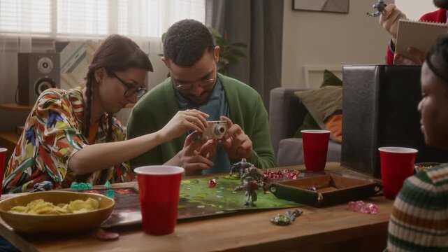Two friends taking picture with camera while enjoying board game get-together with friends in cozy living room