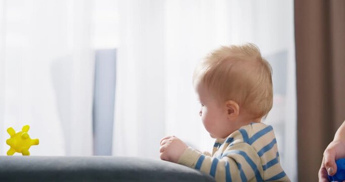 A toddler wearing striped pajamas playing and exploring toys with the guidance of an adult in a softly lit, cozy indoor setting during daytime
