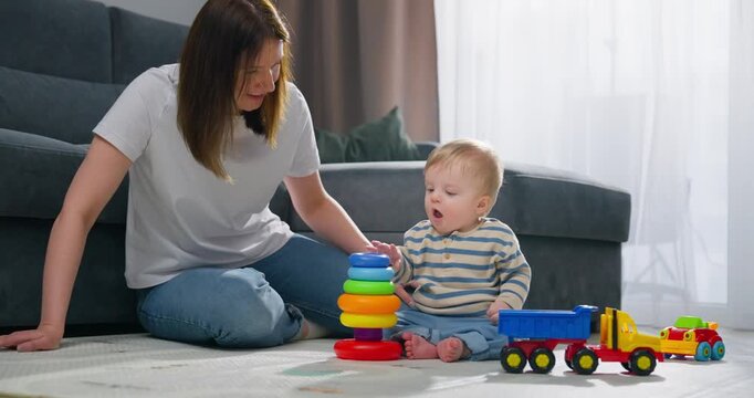 A mother and her baby playing together on the floor with colorful stacking rings and toy vehicles in a bright living room, fostering early childhood development and bonding