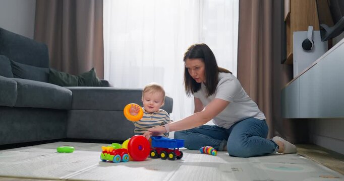 Mother and baby playing together on the floor with colorful toy cars and stacking rings in a cozy living room setting, fostering early childhood development and bonding