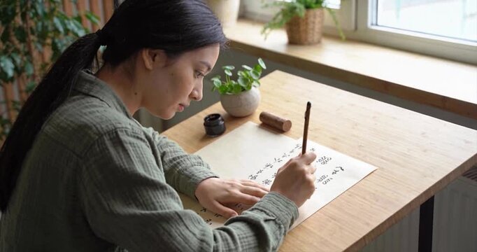 Woman writing calligraphy on paper near window
