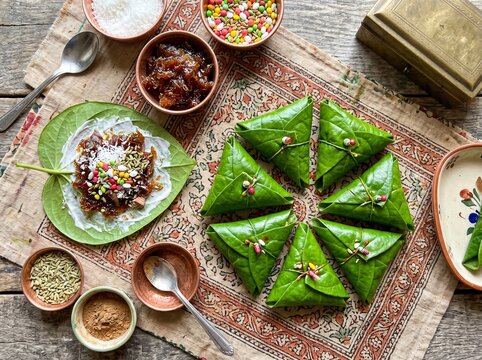 Beautifully arranged fresh green paan betel leaves folded into triangles on a traditional wicker tray with colorful filling ingredients including gulkand, fennel seeds, coconut, and sweet toppings.
