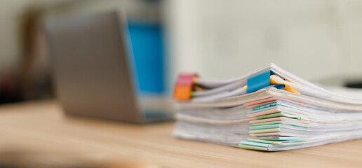 Stack of document files, paperwork, and reports organized with binder clips on a desk next to a blurred laptop, representing business management and data organization © David