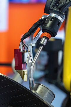 Industrial robotic arm equipped with a precision sensor and welding wire feed head, demonstrated at an indoor industrial technology exhibition.