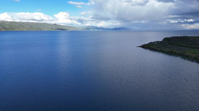 4K Drone Aerial View of Calm Mountain Lake With Green Hills Beneath Atmospheric Clouds.