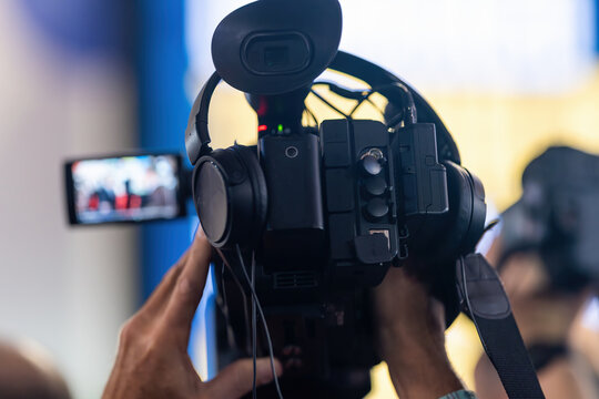  Live media coverage captured from behind as a cameraman operates a professional video camera at an indoor public event.