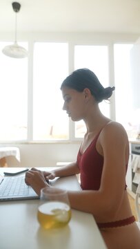 Casual woman working on laptop with juice nearby in sunny kitchen