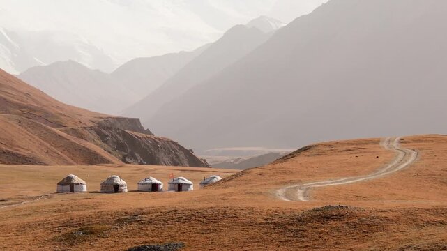 Traditional yurt camp in Achik-Tash valley, Kyrgyzstan. Row of nomadic tents near Lenin Peak with a winding mountain road and majestic Pamir mountains in background
