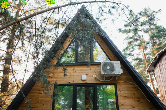 A-frame log chalet house in the forest with a natural backdrop. Summer getaway in a wooden cottage. Outdoor terrace, seating area, firewood