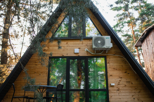 A-frame log chalet house in the forest with a natural backdrop. Summer getaway in a wooden cottage. Outdoor terrace, seating area, firewood