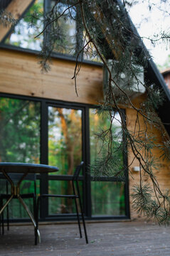 A-frame log chalet house in the forest with a natural backdrop. Summer getaway in a wooden cottage. Outdoor terrace, seating area, firewood