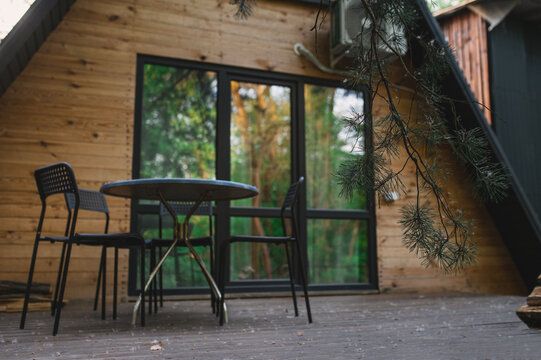 A-frame log chalet house in the forest with a natural backdrop. Summer getaway in a wooden cottage. Outdoor terrace, seating area, firewood
