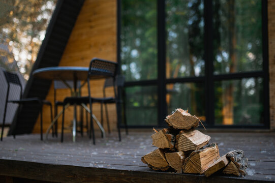 A-frame log chalet house in the forest with a natural backdrop. Summer getaway in a wooden cottage. Outdoor terrace, seating area, firewood