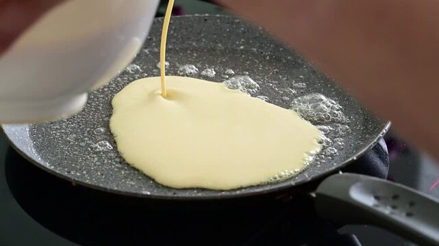 Extreme close up slow motion footage of melted butter bubbling across a hot frying pan surface before crepe batter is poured in. Detailed view of the cooking process in a home kitchen.