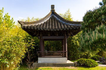 Fototapeta premium Front view of a beautiful pagoda against the blue sky and green trees in Chinese garden in a public park