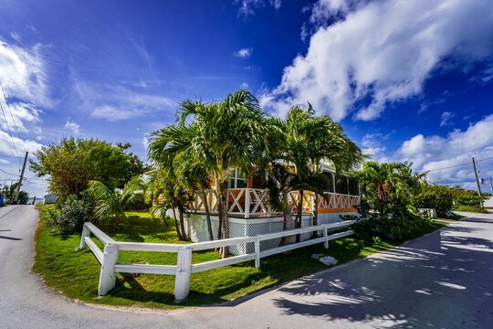 Colorful tropical beach house surrounded by lush palm trees under a dramatic blue sky on Great Guana Cay, Bahamas. Charming Caribbean island lifestyle and vacation destination in the Abaco Islands.