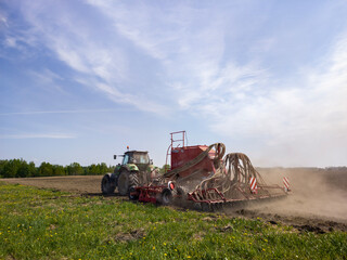 Fototapeta premium Tractor pulling a seeder machine across a field. Farmer planting seed in soil during spring season. Modern agricultural equipment