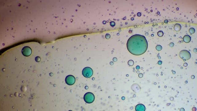 Abstract macro photography of a yellow fluid boundary and scattered blue-green drops on a light background
