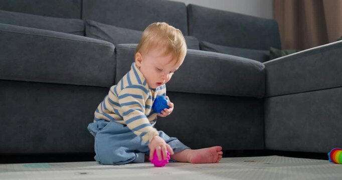 A toddler playing and exploring colorful textured balls while sitting on the floor in a cozy living room, demonstrating curiosity and motor skill development through tactile play.