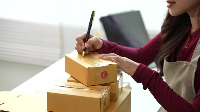 Online seller writing shipping information on a package at a home workspace, representing order fulfillment, e-commerce operations, and small business logistics.