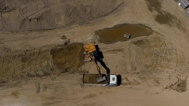 Drone view of an excavator loading soil into a dump truck at a construction site in northern Italy. Earthmoving operations support infrastructure development, site preparation and civil engineering pr