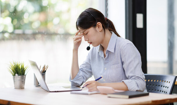 Asian customer service representative experiencing stress and headache, working at a call center, feeling overwhelmed and fatigued from demanding work