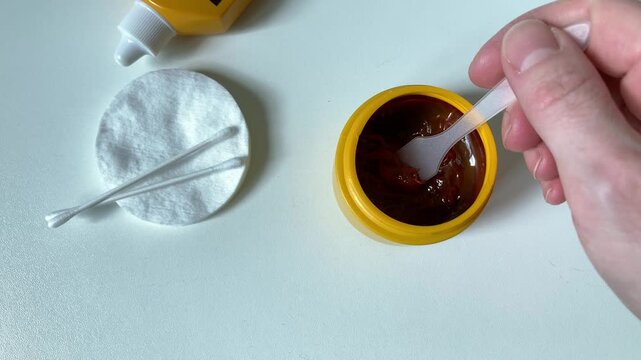 A woman puts iodine ointment on a cotton swab, preparing to treat a cut or minor skin injury. The importance of timely disinfection of damage to prevent infection