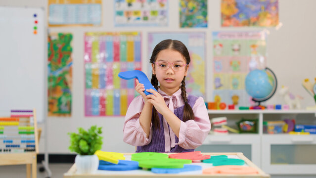 Young Asian Girl Holding Foam Number in Bright Elementary Classroom Setting