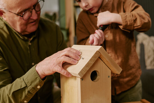 Senior man and child assembling wooden birdhouse, guiding screwdriver work and hands on craft project. Family bonding and practical learning concept for parenting or education campaigns