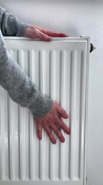 Vertical video. A woman checks the radiator in winter to make sure there is heat. The theme of seasonal life, taking care of the warmth in the house during the cold season