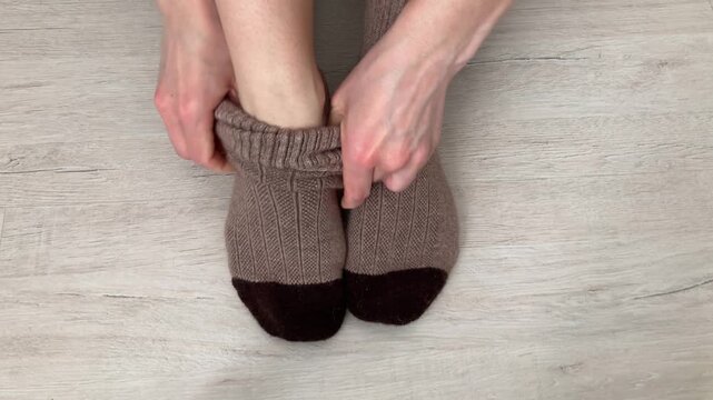 A woman puts on warm wool socks, struggling with household difficulties in winter. Lack of heating in the apartment during the cold season