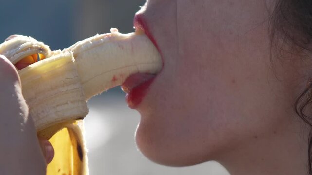 Banana eating woman with red lips bites fruit in a suggestive close-up outdoor scene